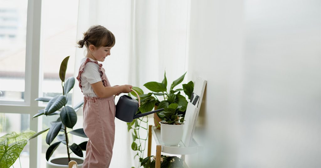 Young girl watering plants inside home