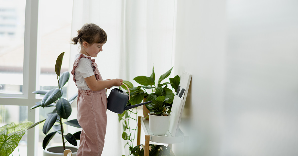 Young girl watering plants inside home
